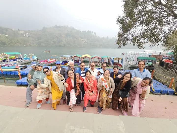 Joyful traveler group smiling at Bhimtal lakeside with paddle boats in background